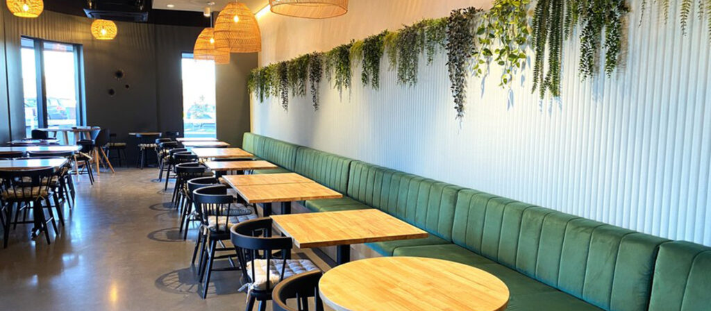 Contemporary Thai eatery with a cozy green bench, cascading greenery, soft lighting, and a mix of square and round tables.