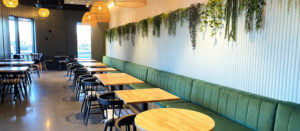 Contemporary Thai eatery with a cozy green bench, cascading greenery, soft lighting, and a mix of square and round tables.