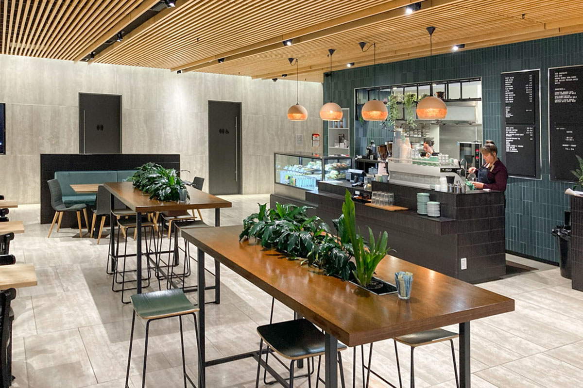 Moji-Coffee-2 Bright open-plan interior office fit out with modern workstations, large windows, ergonomic chairs, and green and grey patterned carpet.